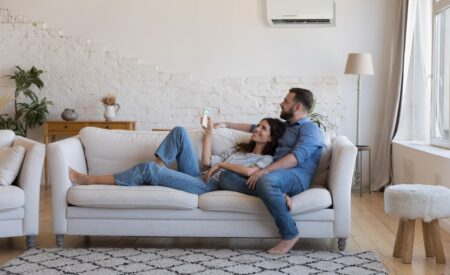 A Couple Comfortably Lies On Their Living Room Couch, Enjoying The Advantages Of Their New Lennox Air Conditioner.