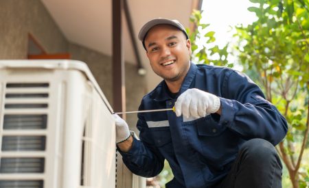 A Smiling Professional HVAC Technician Performs Essential AC Maintenance Tasks For A Homeowner, Making Sure They Are Ready For The Spring And Summer Seasons.