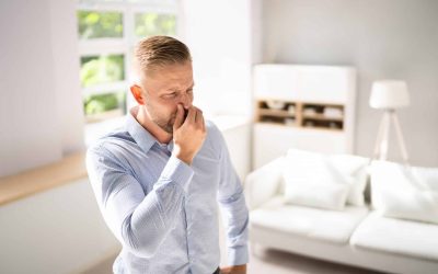 A Man Stands In His Home, Hand Covering His Mouth, Reacting To An Unpleasant Odor From The Air Conditioning System.