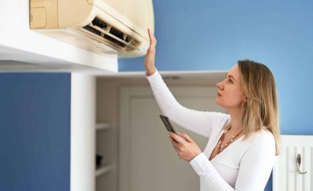 A woman holding a remote control appears frustrated as she tries to reset her air conditioning unit.