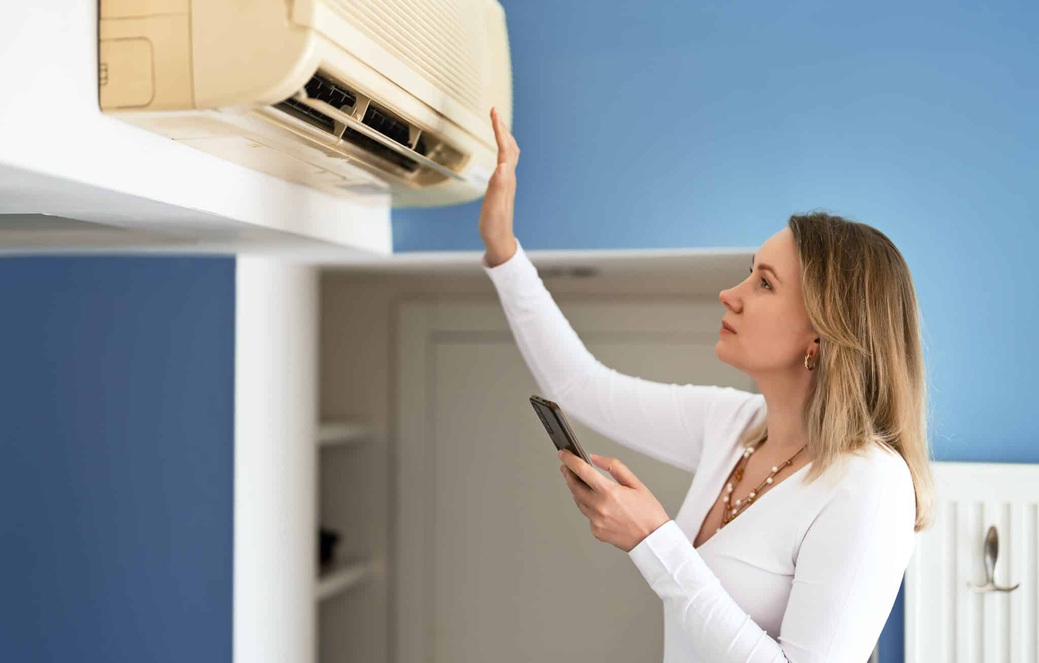 A woman holding a remote control appears frustrated as she tries to reset her air conditioning unit.