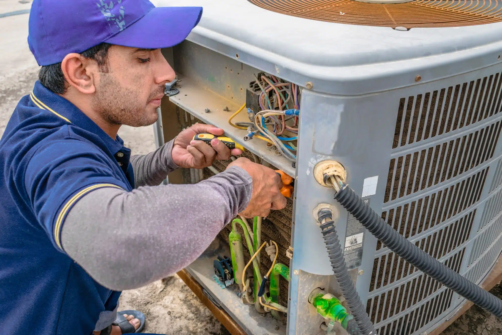 An HVAC technician works diligently to repair an air conditioner for a homeowner in the middle of a heatwave.