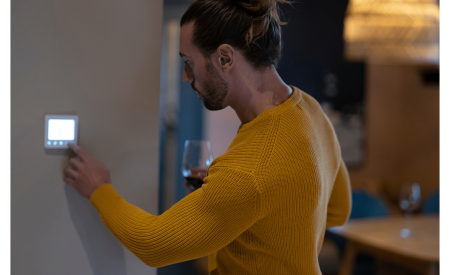 Man in a yellow shirt adjusts the smart thermostat at a modern home.
