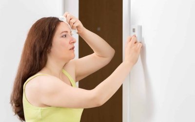 A woman tries to set the temperature on a non-responsive wall thermostat during an AC emergency.