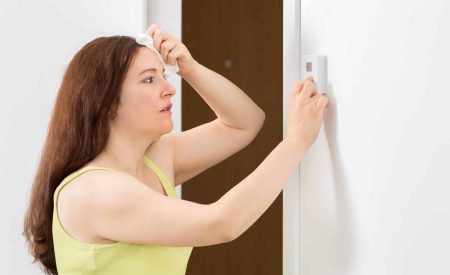 A woman tries to set the temperature on a non-responsive wall thermostat during an AC emergency.