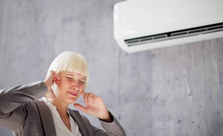 Woman covers her ears as she walks past a noisy air conditioner