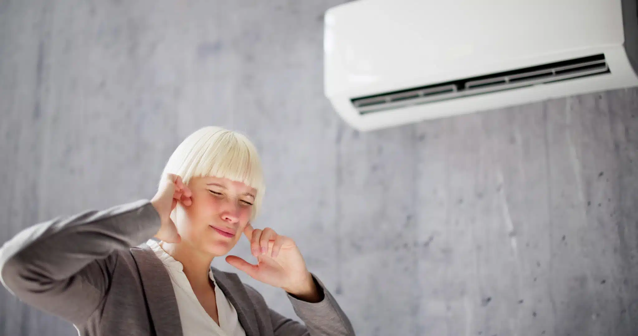 Woman covers her ears as she walks past a noisy air conditioner