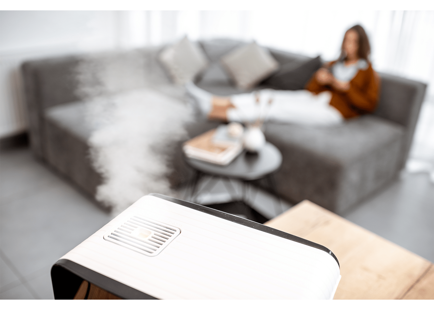 A female homeowner relaxing on the couch while enjoying the comfort of a humidifier in the living room.