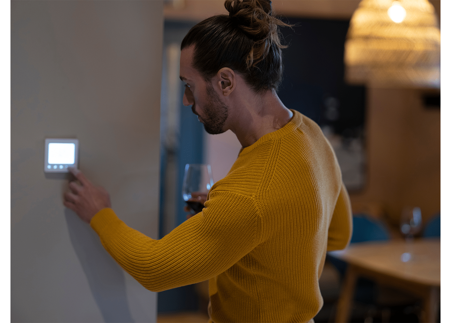A man in a long-sleeved yellow shirt adjusts a smart thermostat in a modern home.