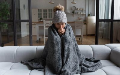A woman wrapped in a blanket on a couch attempts to stay warm after her HVAC system struggles during a winter cold snap.