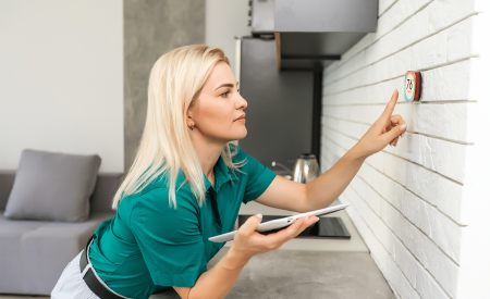 Smart home digital thermostat touch screen woman touching touchscreen to adjust temperature of heating in living room wall