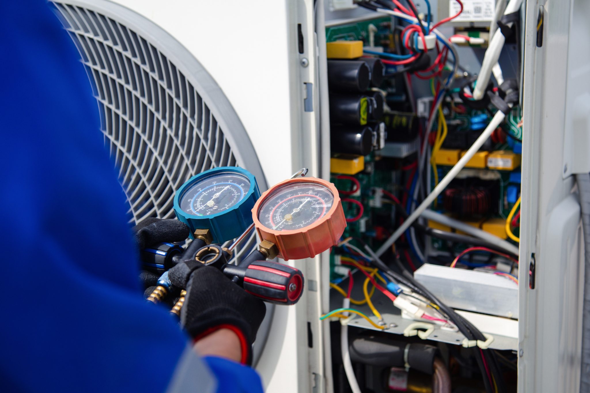 HVAC technician checking an outdoor AC unit with refrigerant gauges during a spring maintenance AC tune-up.