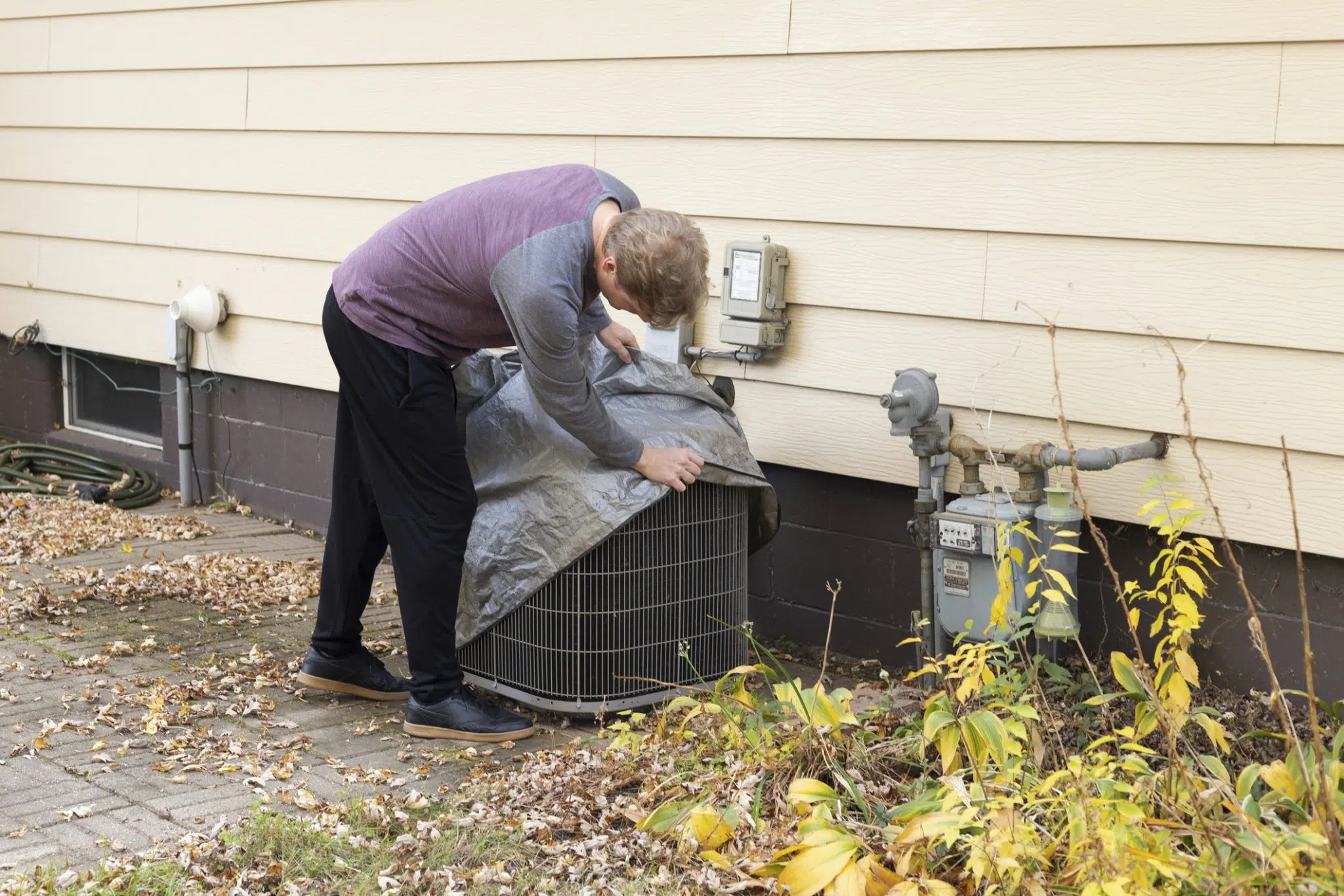 DFW homeowner uncovering an outdoor AC unit as part of spring HVAC preparation before warm weather arrives in North Texas.