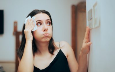 A frustrated DFW homeowner wiping sweat from her forehead while checking her thermostat as her AC cycles on and off.