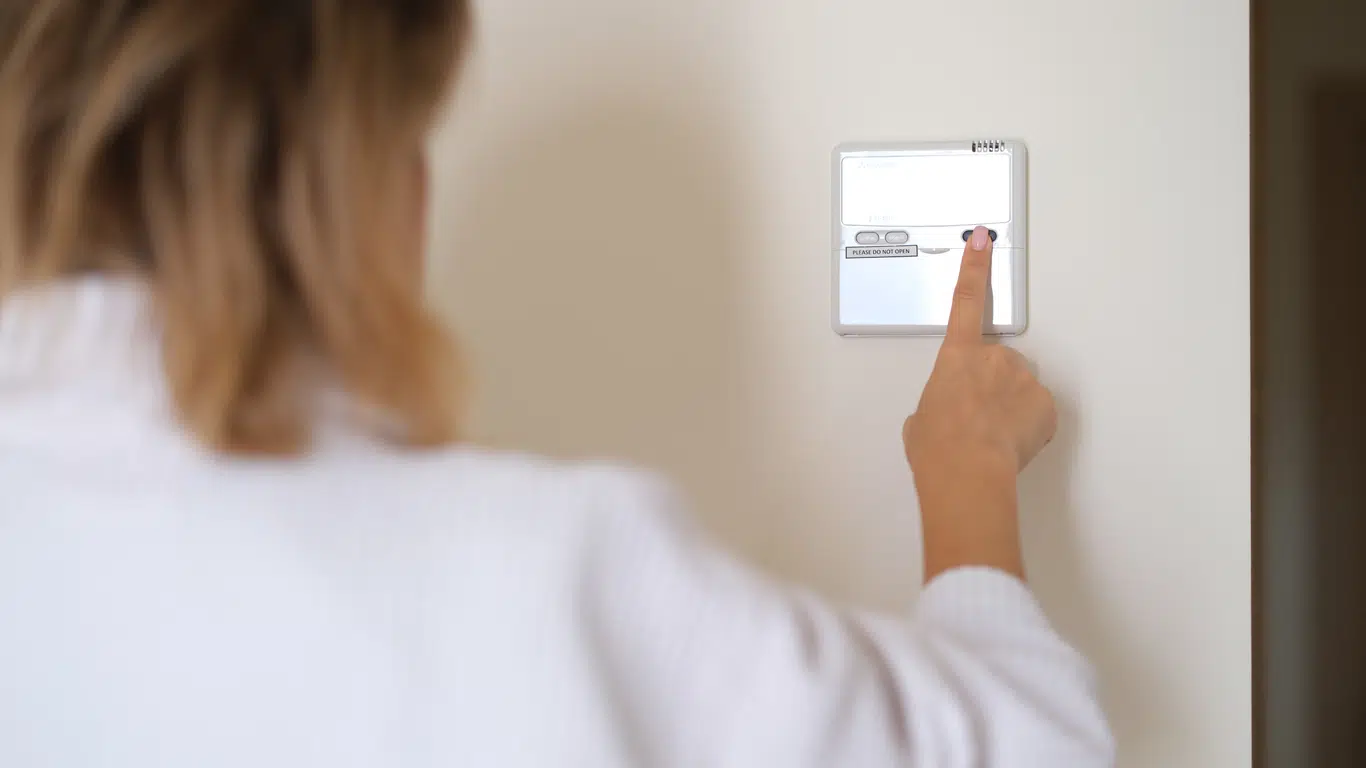 A DFW homeowner adjusting her thermostat to cool her home during spring weather.