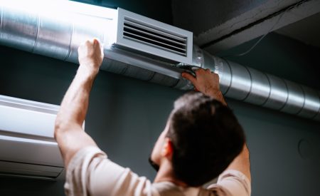 An HVAC technician inspects the air duct and vent register on the ceiling of a DFW home.