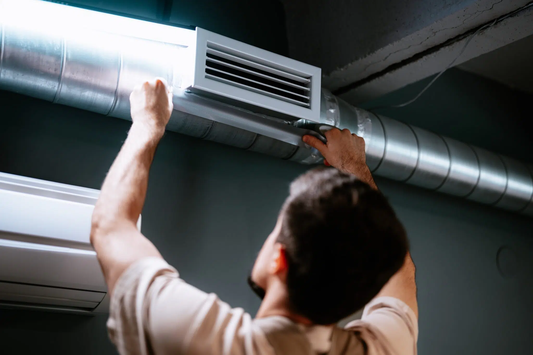 An HVAC technician inspects the air duct and vent register on the ceiling of a DFW home.