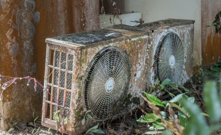 The old rusty and overgrown outdoor split air conditioning system. It is heavily corroded and covered with moss and dirt. timely maintenance of air conditioners and repairs