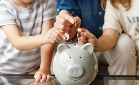 Children and a parent saving coins in a piggy bank, a nod to the money DFW homeowners keep with smart HVAC maintenance tips.