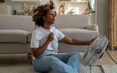 Overheated woman using a fan to cool down in a hot room in her DFW home.