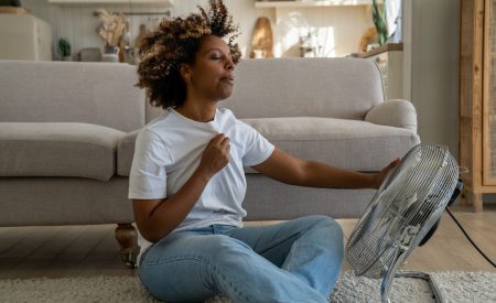 Overheated woman using a fan to cool down in a hot room in her DFW home.