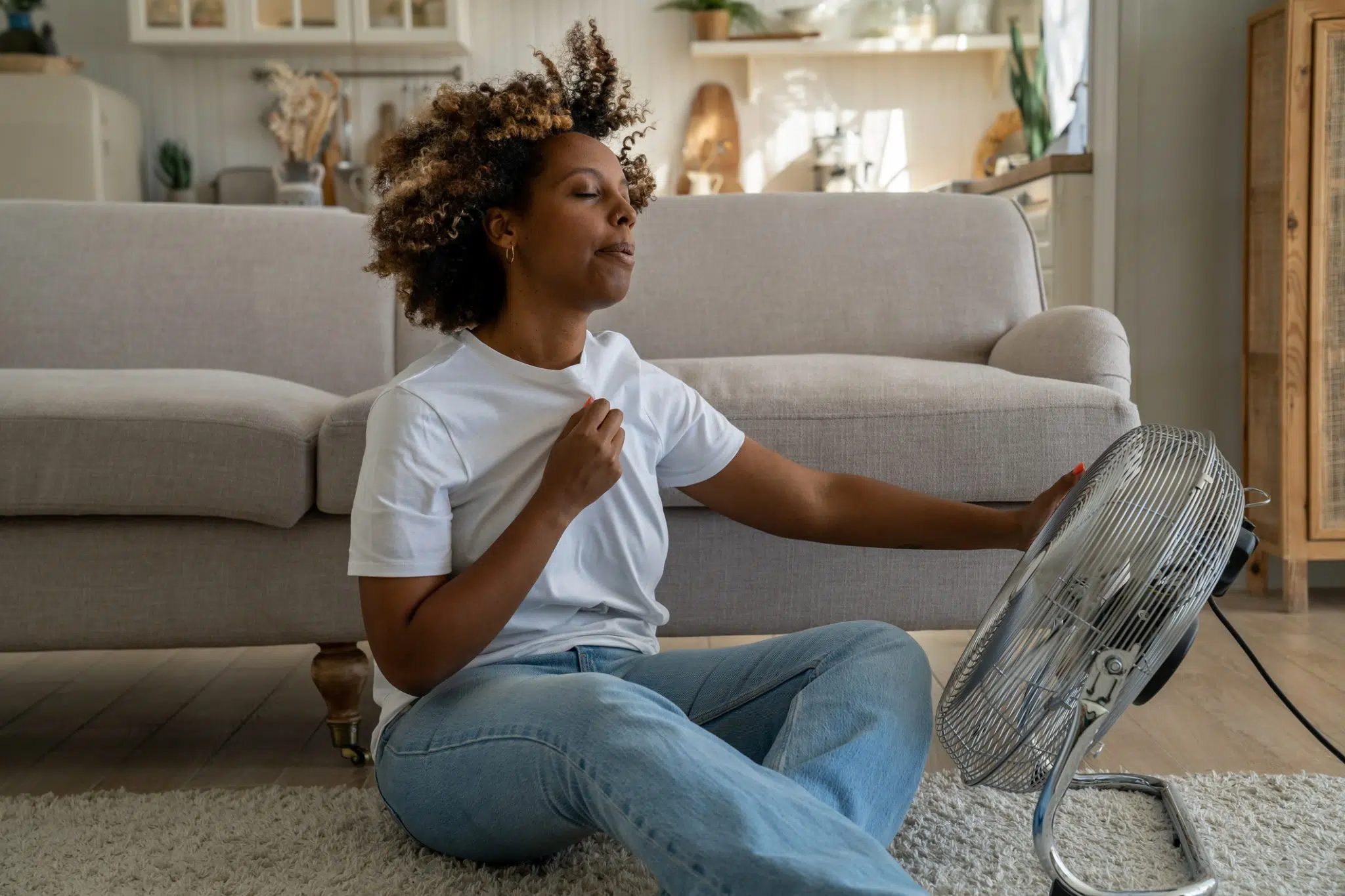 Overheated woman using a fan to cool down in a hot room in her DFW home.