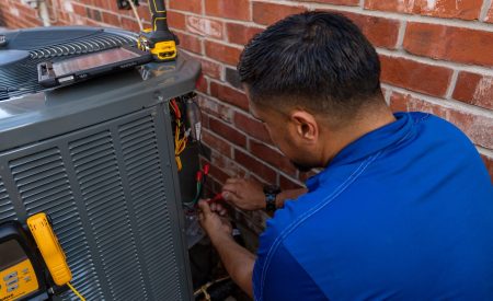 Houk technician performing preventive HVAC service on a central AC unit outside a DFW brick home.
