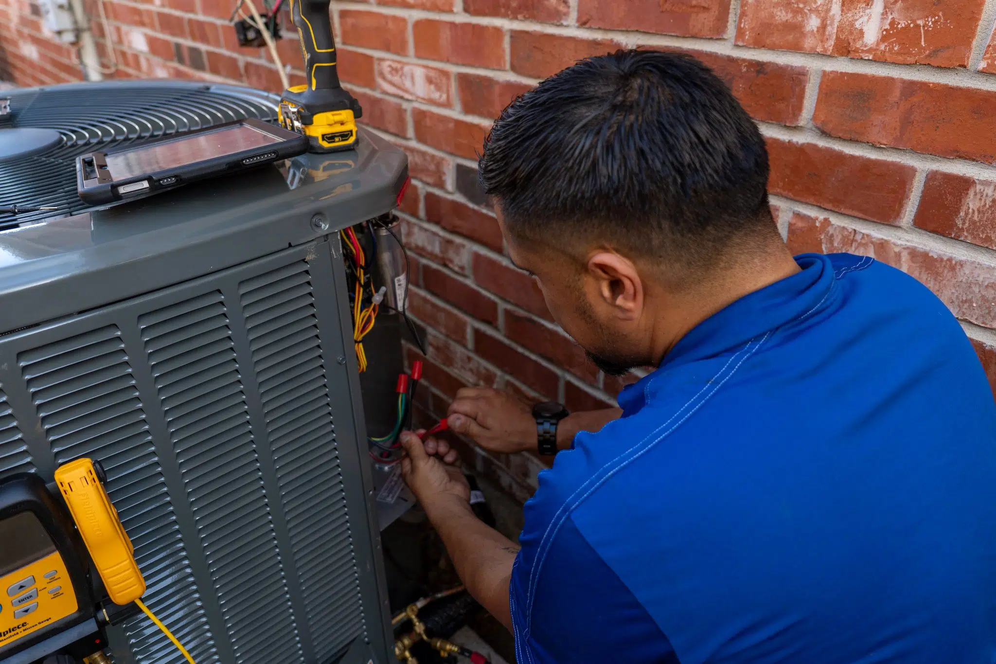 Houk technician performing preventive HVAC service on a central AC unit outside a DFW brick home.
