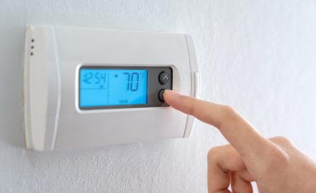 Hand adjusting a home thermostat set to 70°F during an ERCOT conservation alert in Texas.