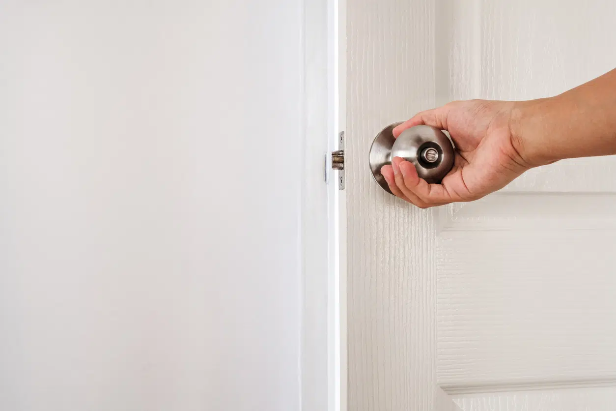 A hand closing a white interior bedroom door, the everyday habit that can restrict a home's airflow