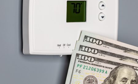 Cash tucked beside a home thermostat, representing what HVAC installation and AC replacement can cost DFW homeowners.